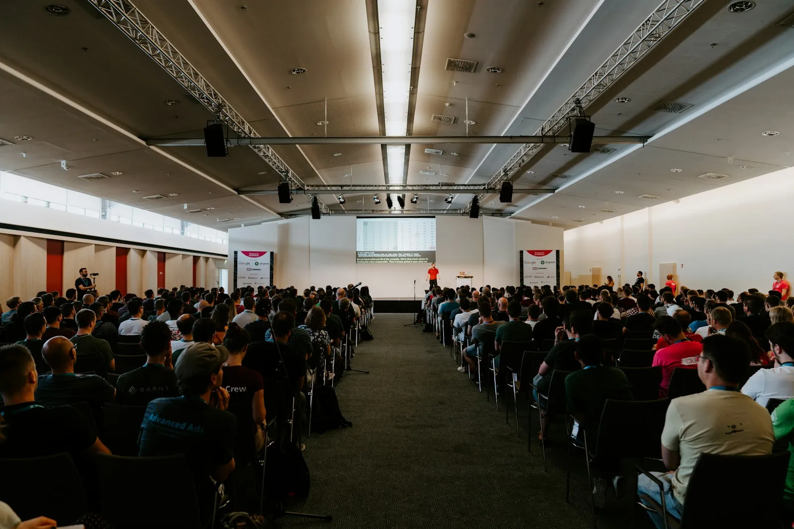 A large conference room filled with hundreds of people seated in rows, facing a stage.